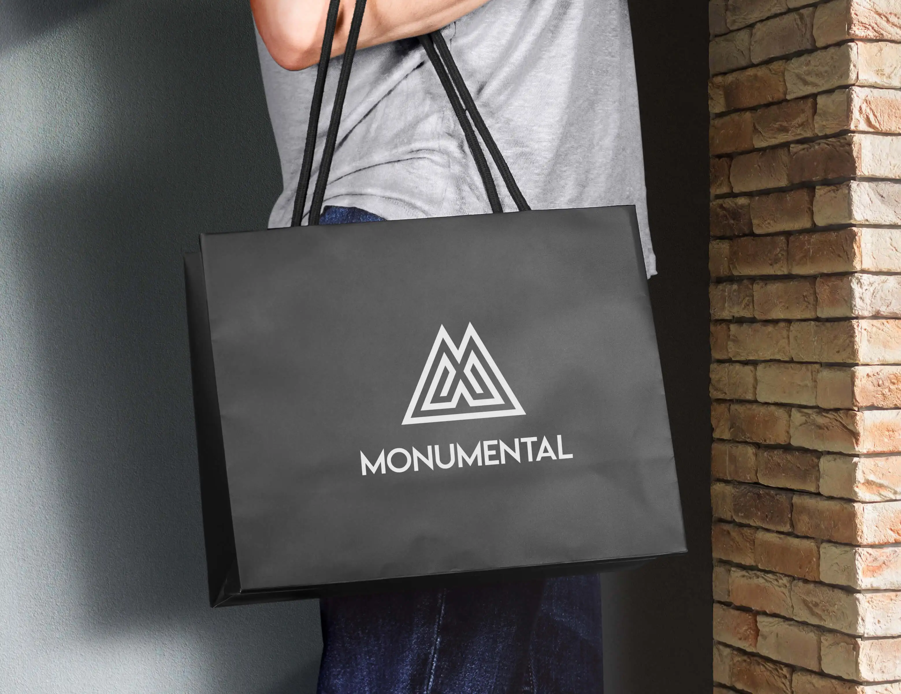 Monumental logo on a black paper shopping bag held in front of brick