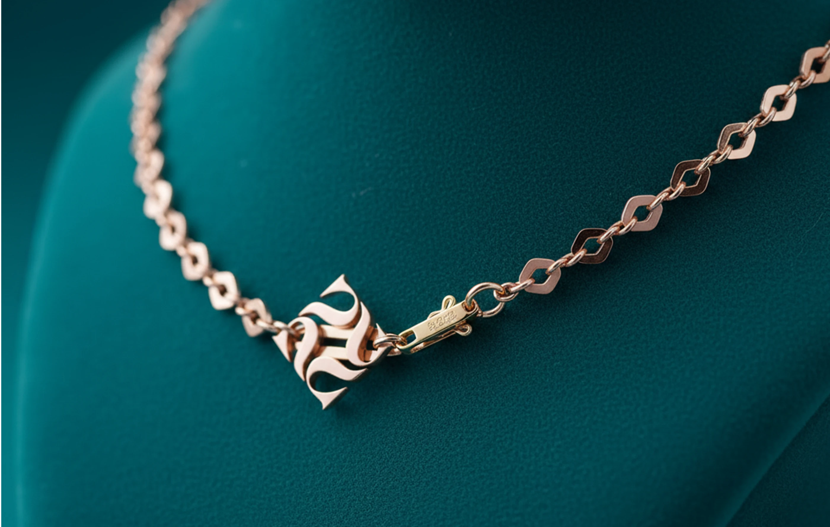 Close-up of a gold chain necklace with the Panna monogram on teal velvet