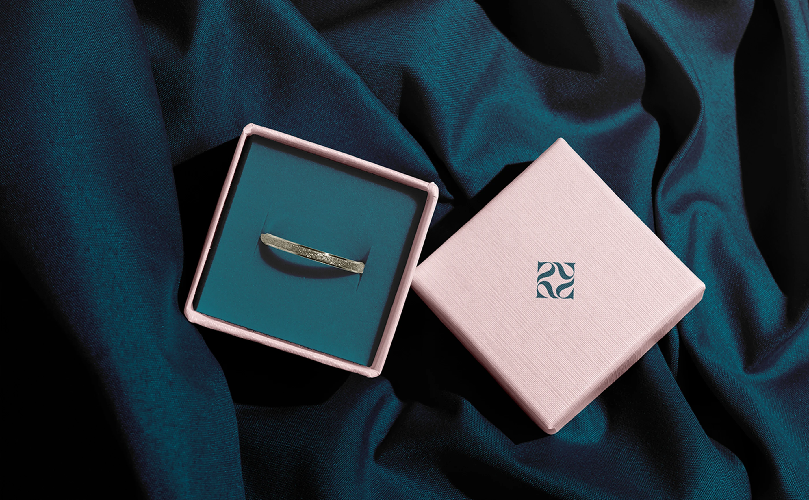 Panna open ring box and a pink gift box on dark teal fabric