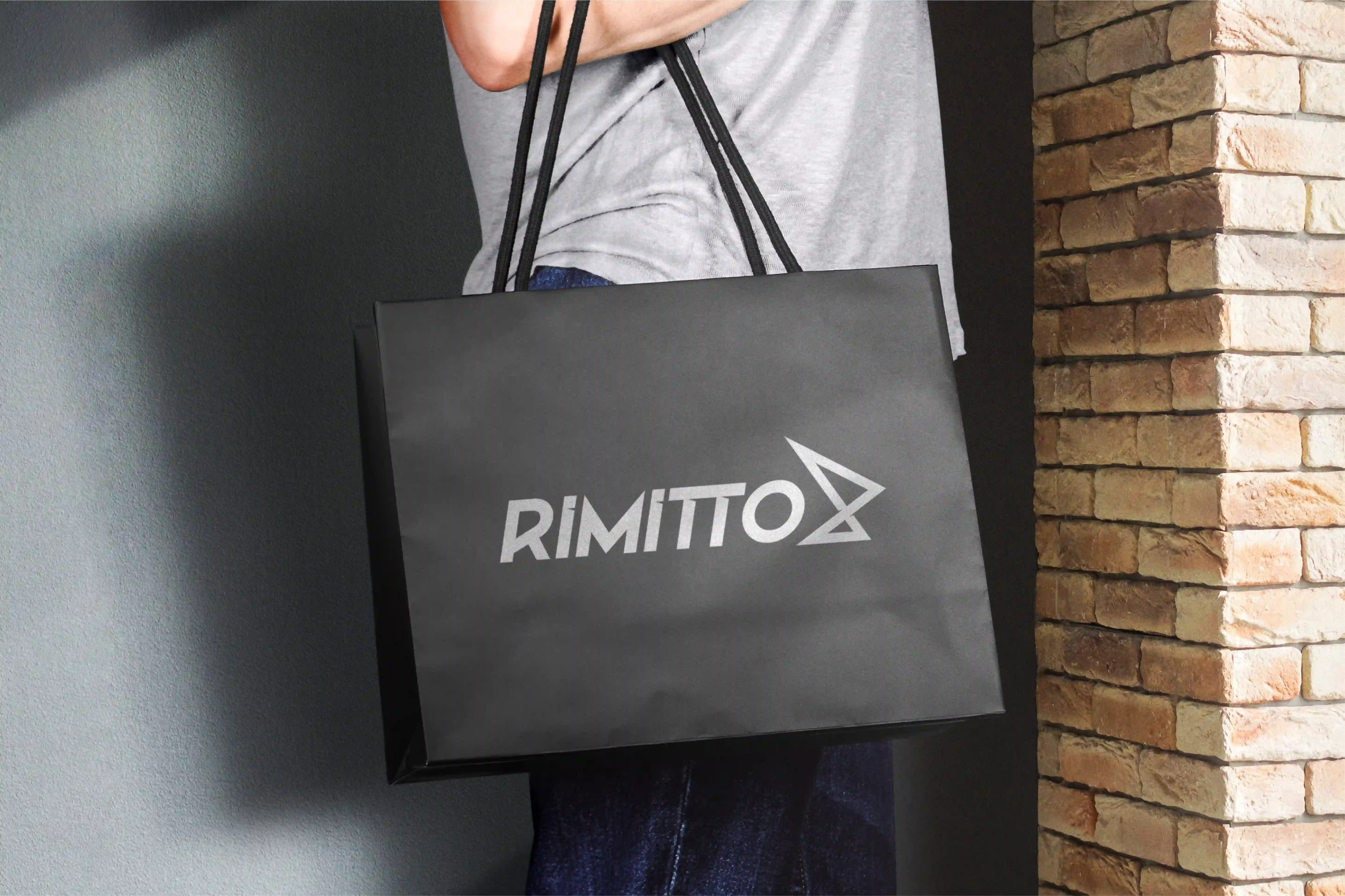 Rimitto logo on a black paper shopping bag held in front of a brick wall