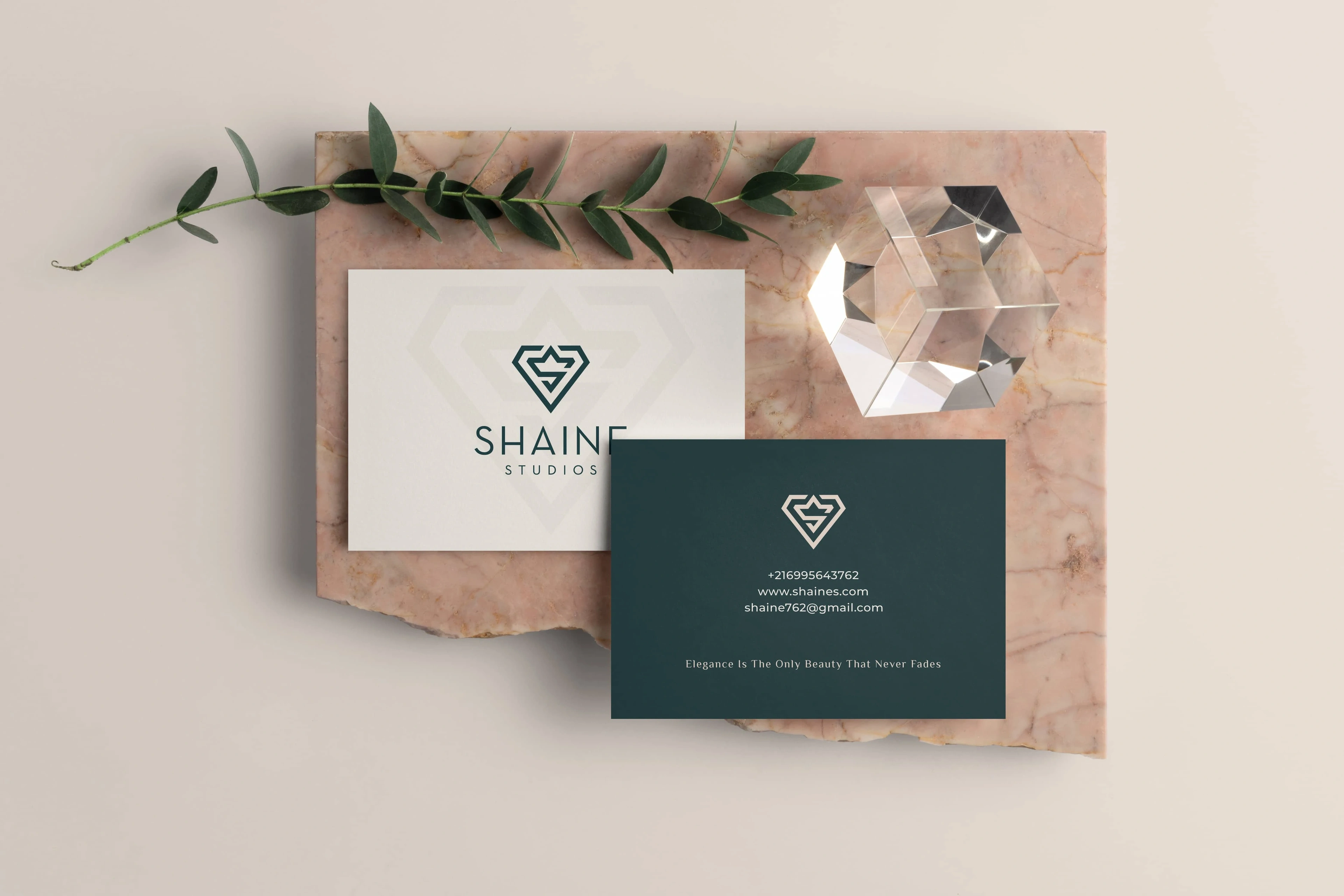 Shaine Studios business cards on pink marble beside a crystal and olive leaves