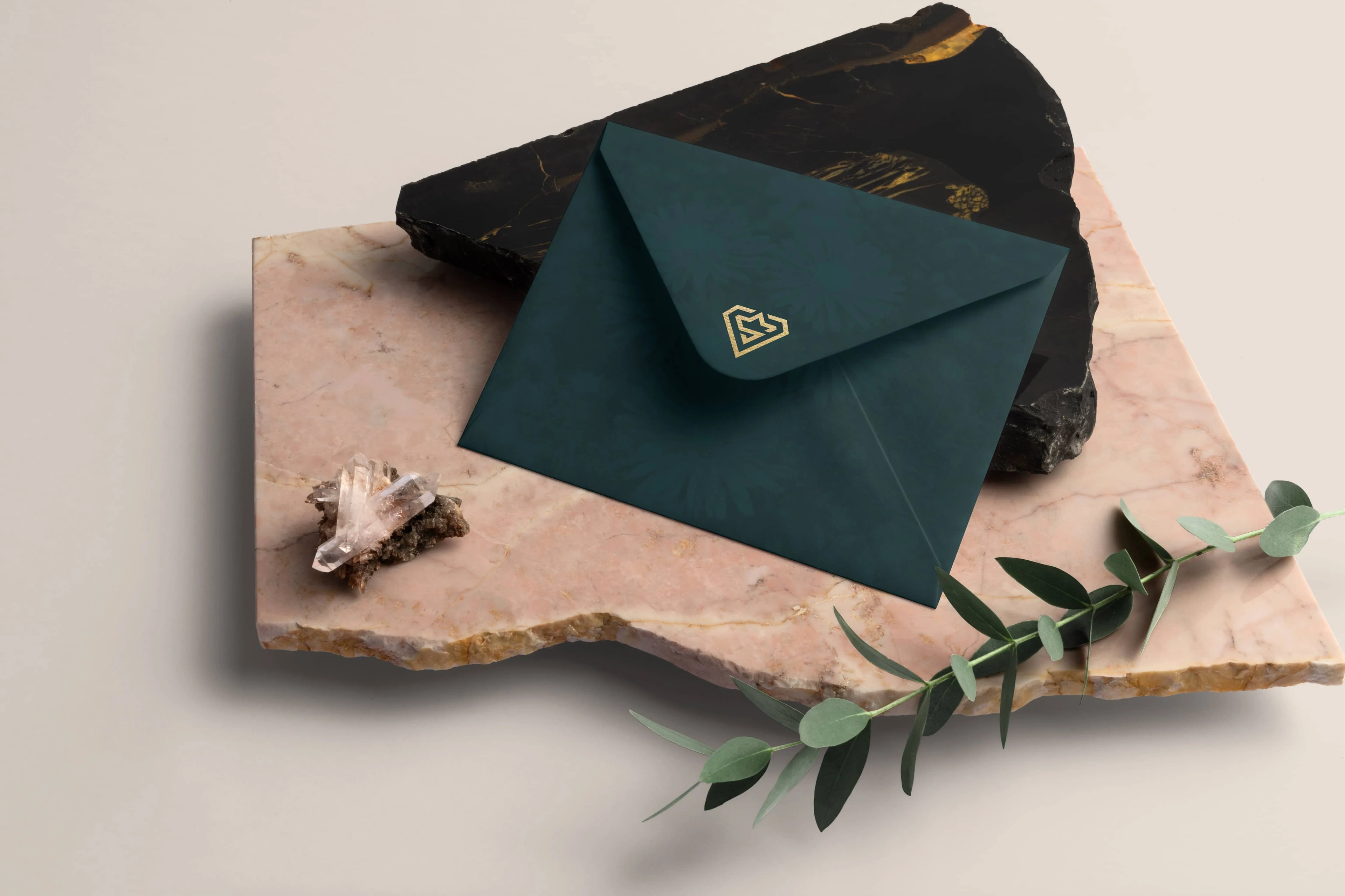 Shaine Studios green envelope with a gold logo on stone and marble slabs with a shell and olive sprig