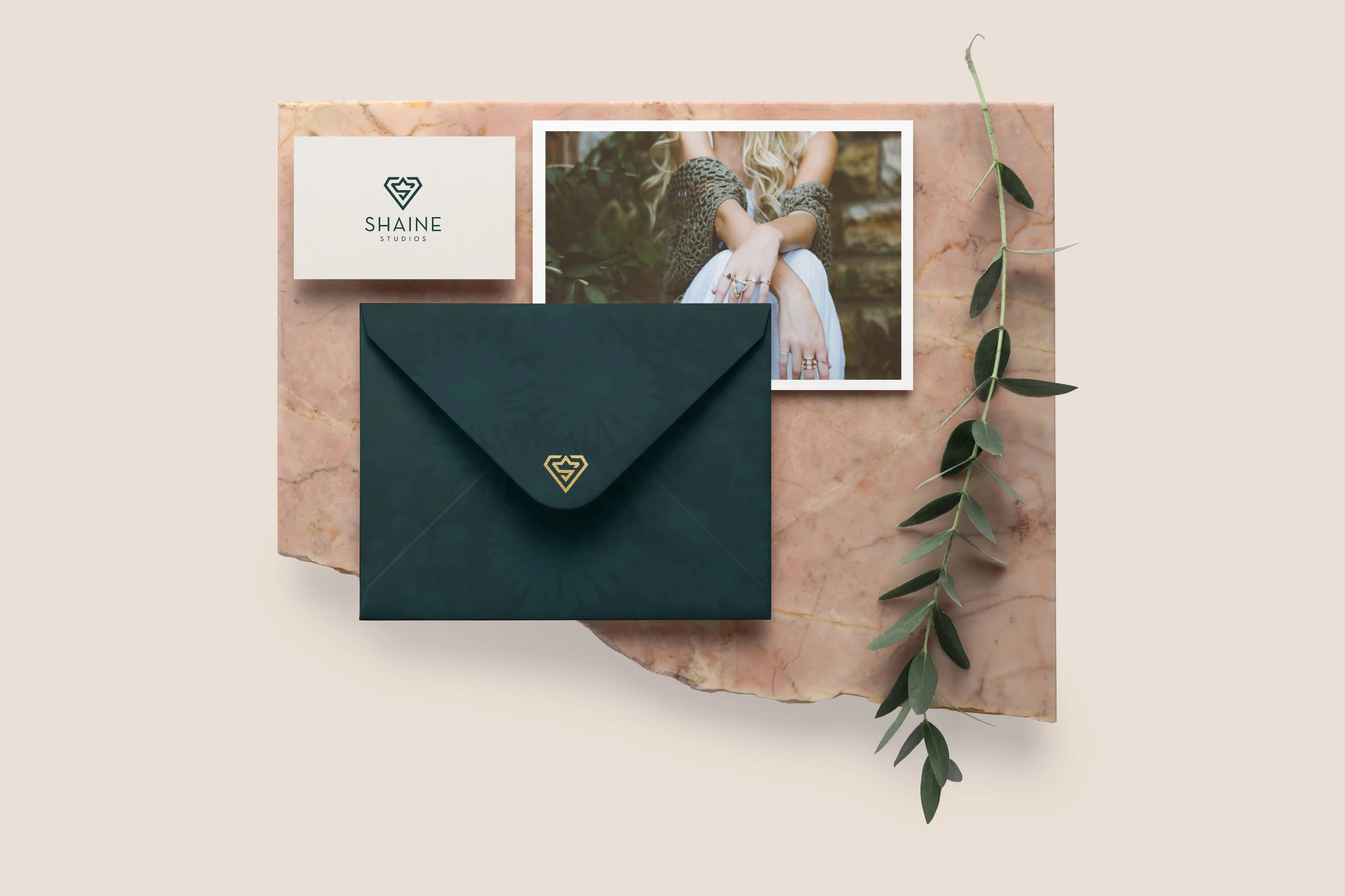 Shaine Studios green envelope, card and photograph on pink marble with an olive sprig