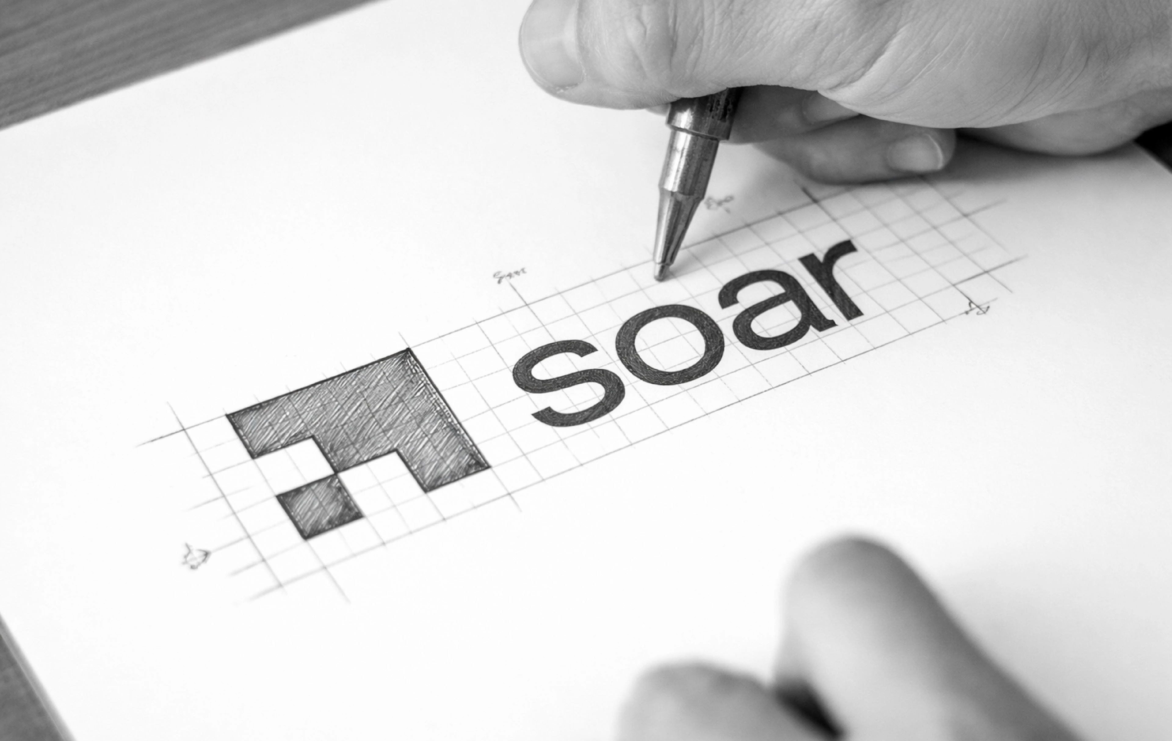 Hand sketching the Soar logo on paper with grid construction lines